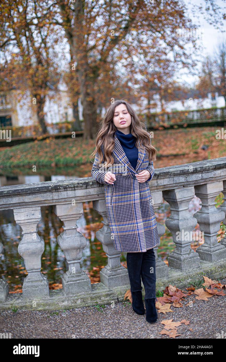 Young woman in trench coat with long curly hair in autumn park standing ...