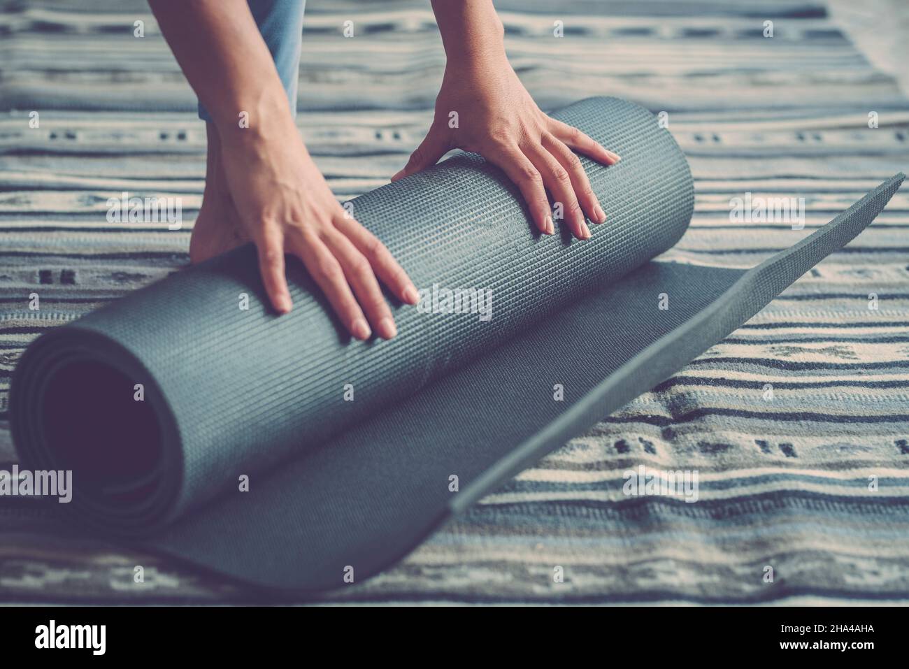 healthy fitness woman hands rolling up mat after exercise on floor in living room,woman doing exercise at home. hands of woman rolling or unrolling yoga mat on floor at home Stock Photo