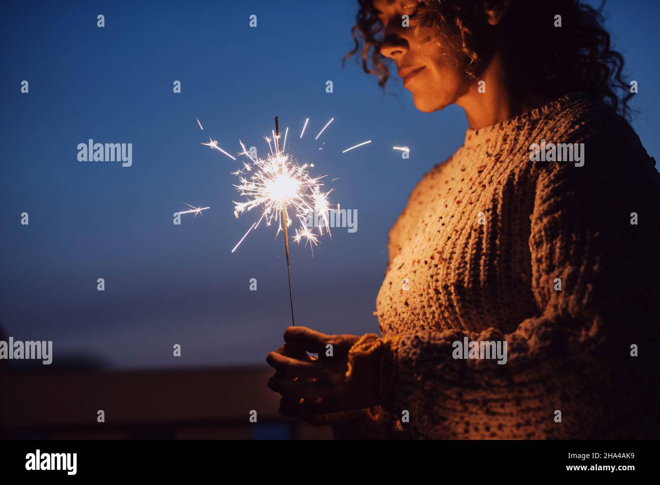 adult woman with closed eyes holding sparkler in the night with blue sky in background - new year eve christmas holidays - female people with firework outdoor enjoy emotions and feeling Stock Photo