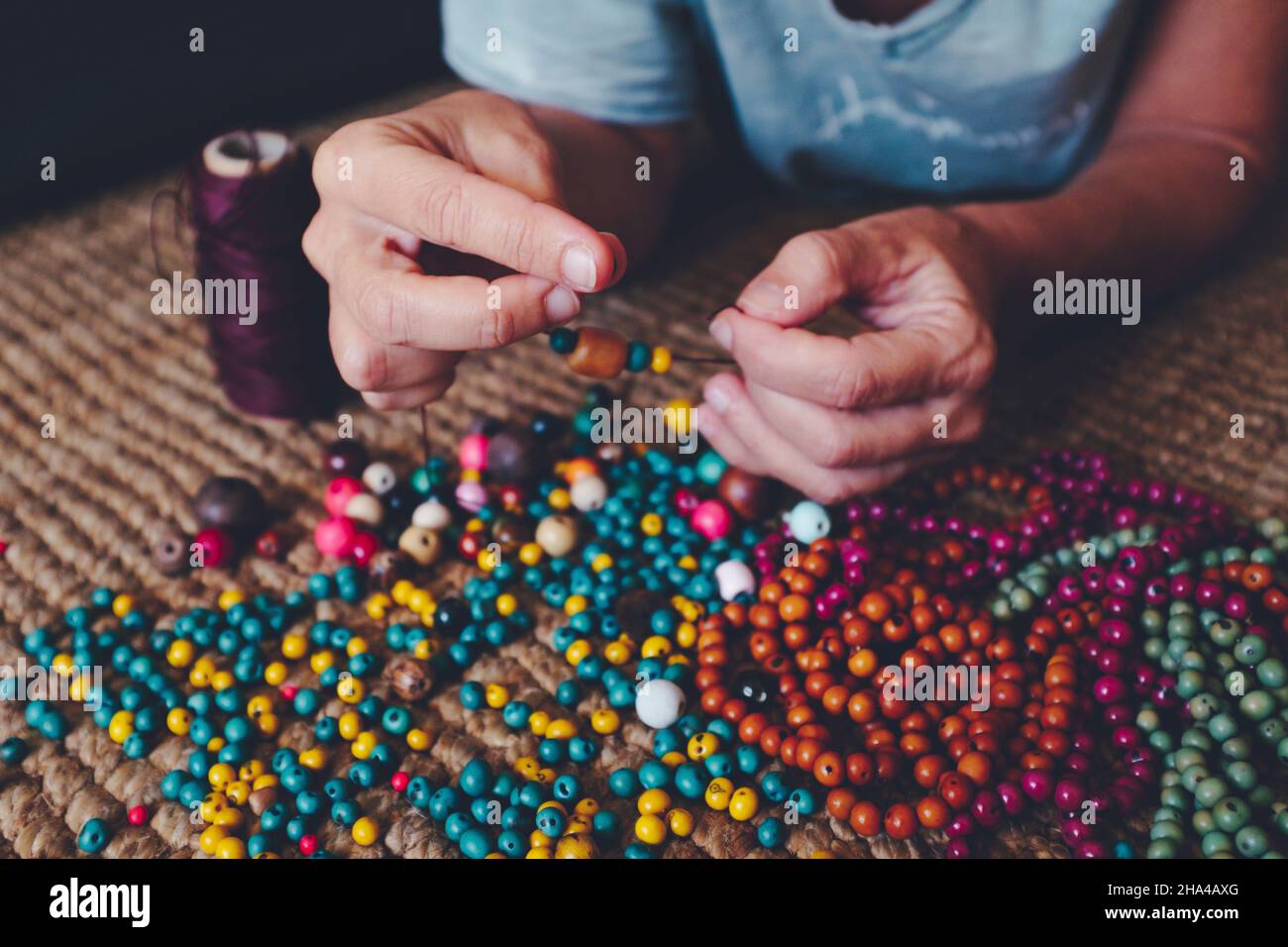 close up of woman hands doing hobby creative beads jewels at home on the carpet. people and diy leisure indoor activity Stock Photo