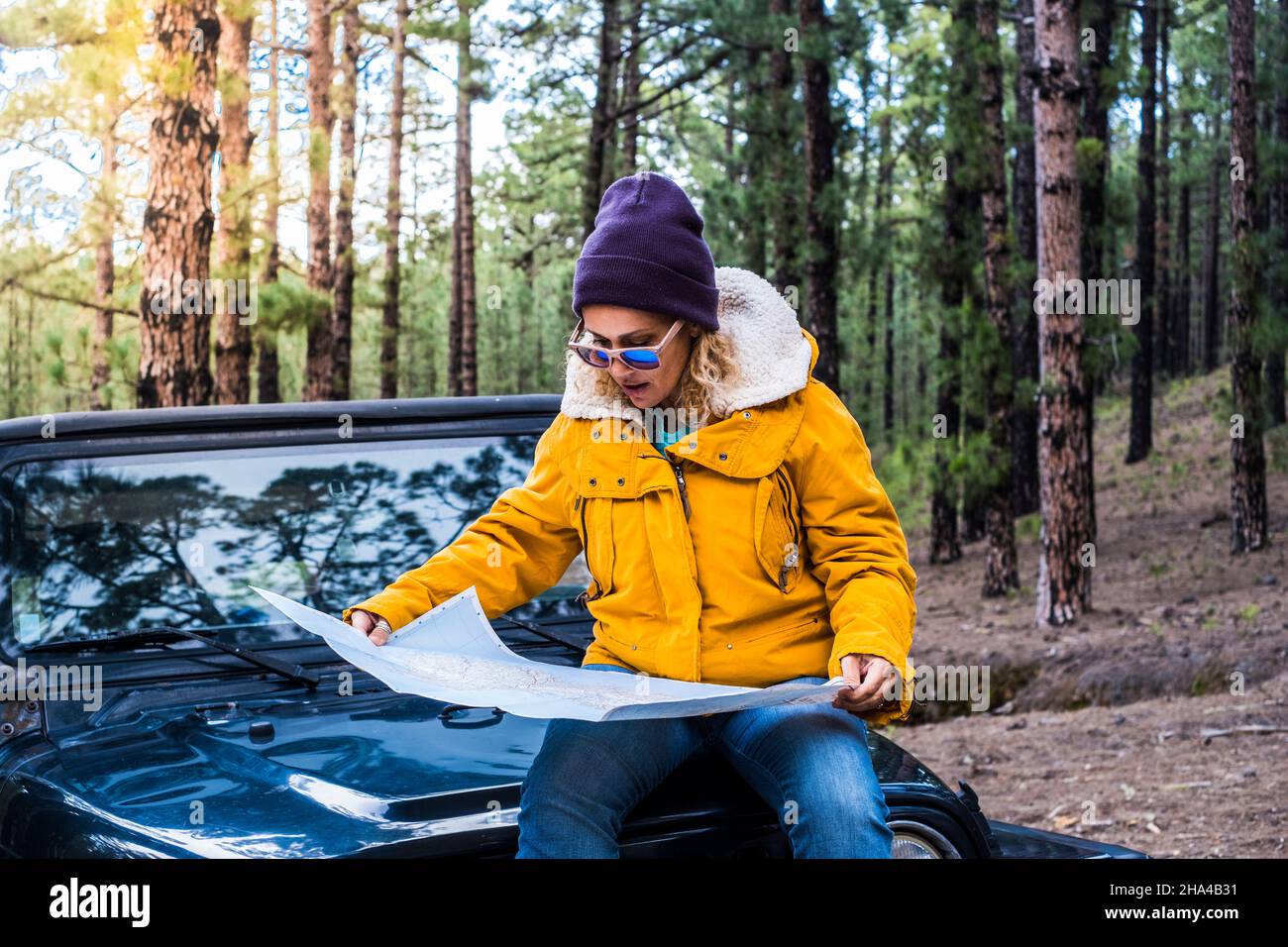 young woman sit down on the car and check map guide in alone travel adventure lifestyle - female people enjoy forest and nature woods driving the car and exploring wild places Stock Photo