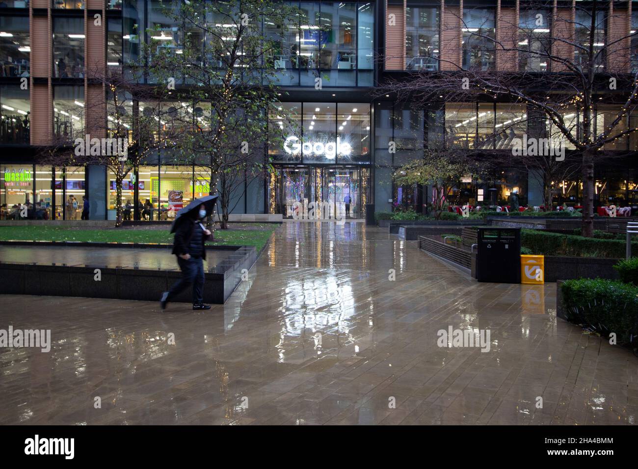 Google offices in Kings Cross London with sign reflected in rain as workers walk past building Stock Photo