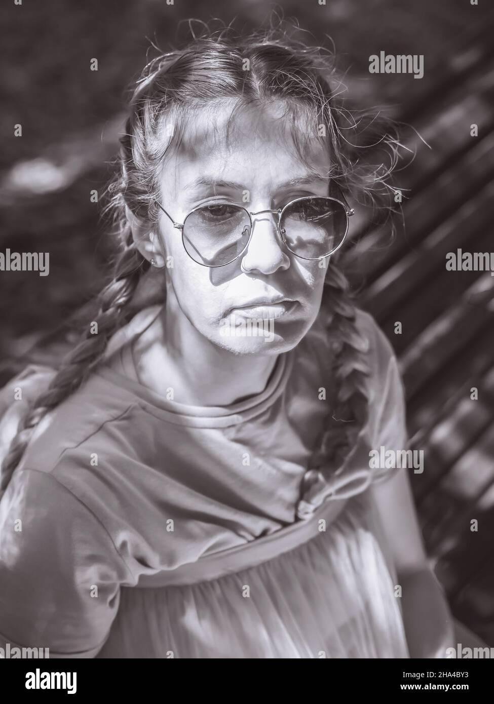 A portrait of sullen lady with two braids sitting on a bench in the ...