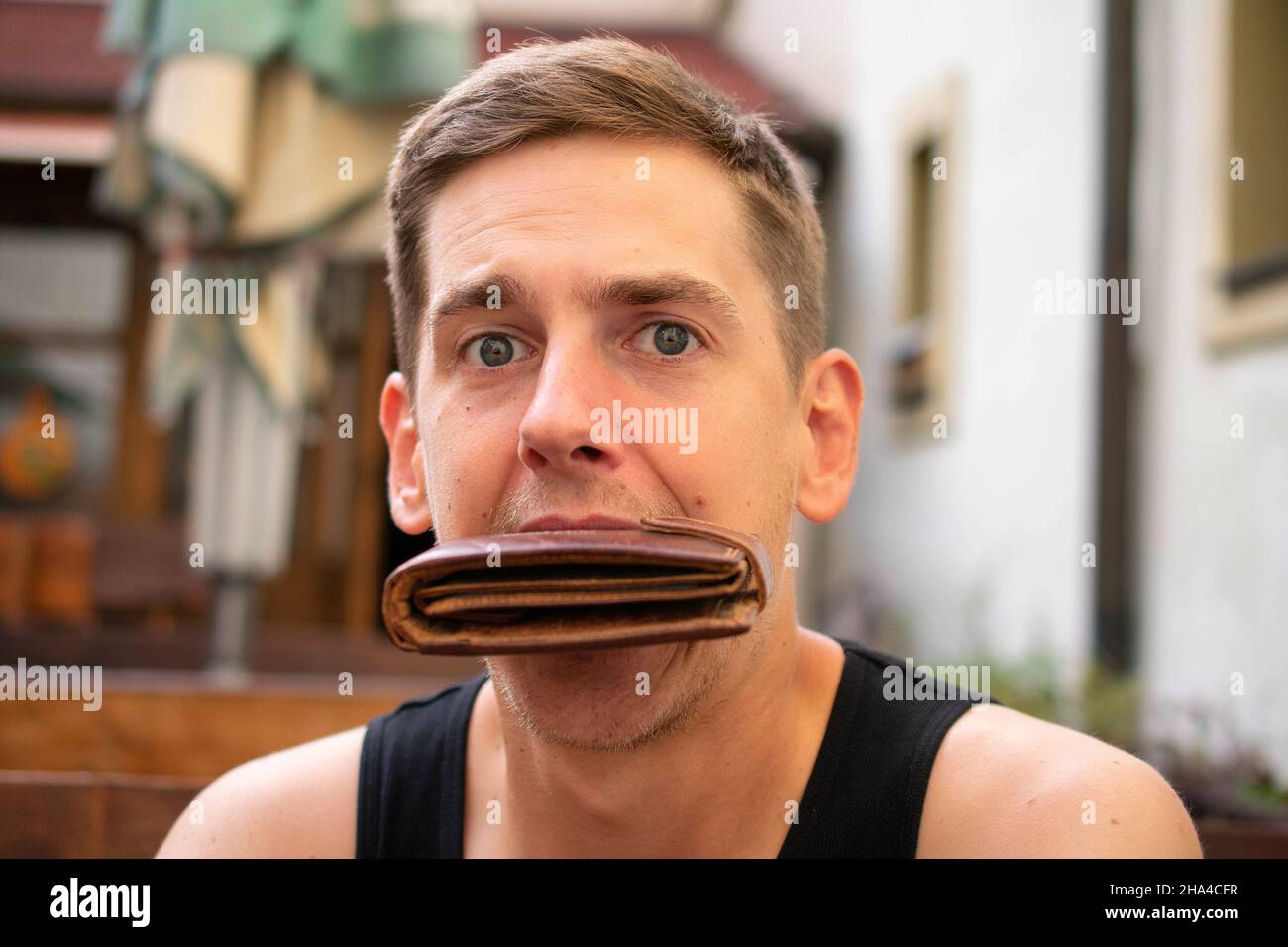 Young handsome white man with brown hair with wallet in his mouth on