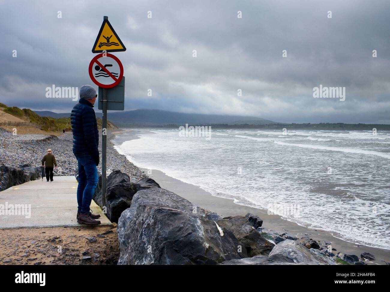 Man standing by danger signs about no swimming at Strandhill beach, Sligo, Ireland Stock Photo