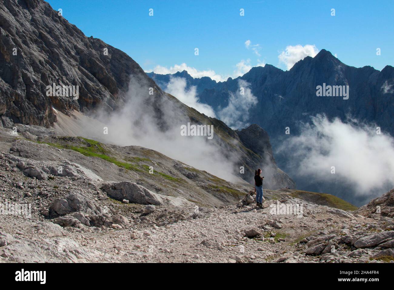 young woman looks at her mobile phone,during a hike to the zugspitze 2962 m,behind it in the picture the hochwanner 2744 m,wafts of fog,wetterstein mountains garmisch-partenkirchen,upper bavaria,bavaria,southern germany,germany,europe, Stock Photo