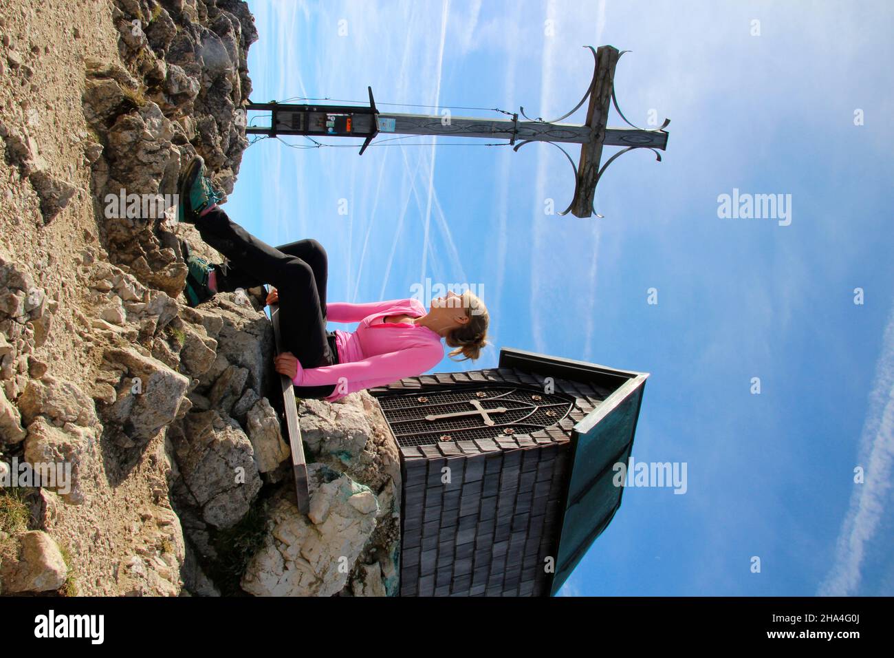young woman takes a break at the summit,hike to geigelstein (1808m),summit cross,chapel,nature reserve,aschau im chiemgau,upper bavaria,bavaria,germany Stock Photo