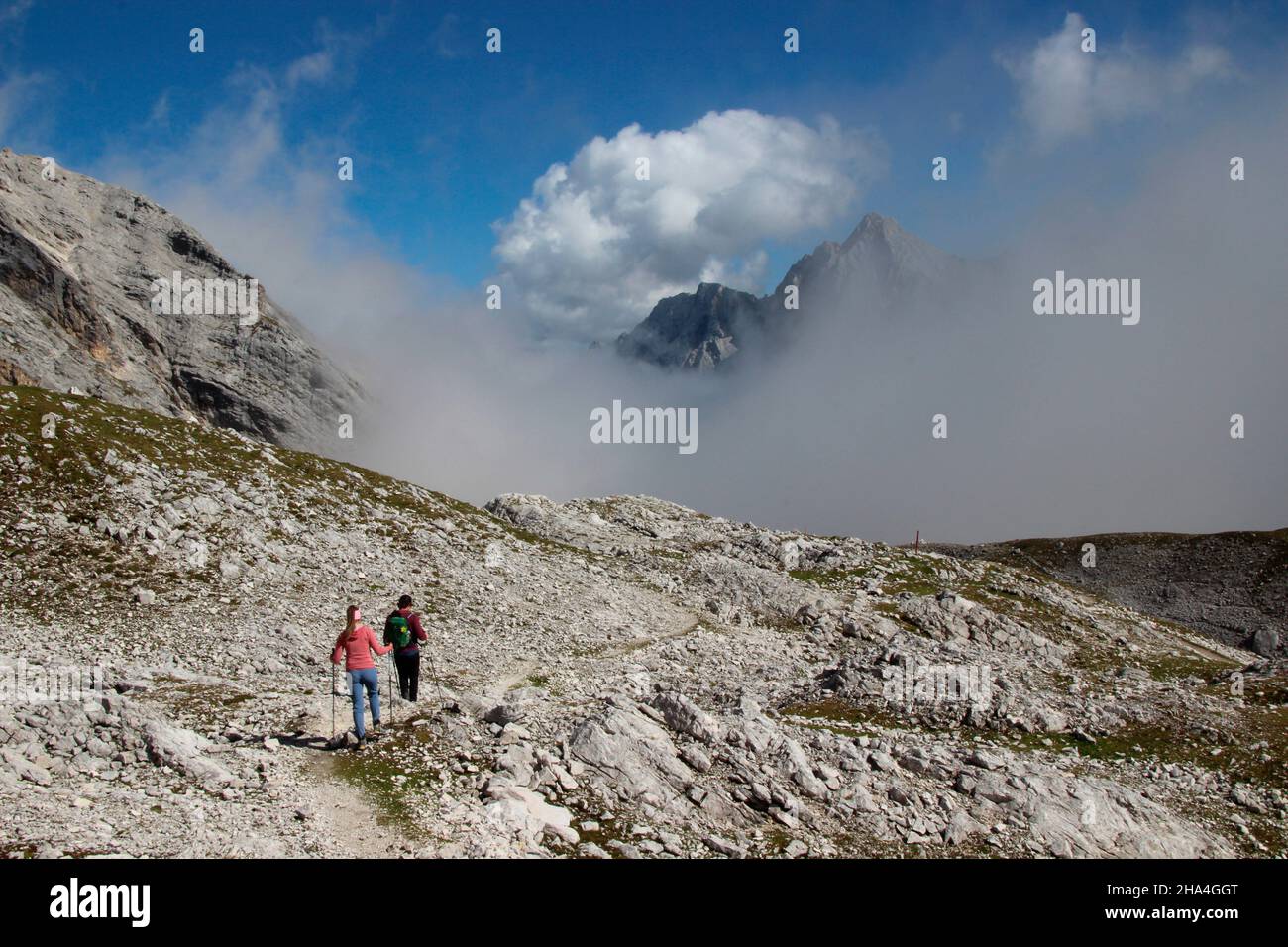 young couple hiking,descent from the zugspitze,wetterstein mountains blue sky,clouds,cloud mood,behind it the summit of hochwanner 2744m,garmisch-partenkirchen,loisachtal,upper bavaria,bavaria,southern germany,germany,europe, Stock Photo