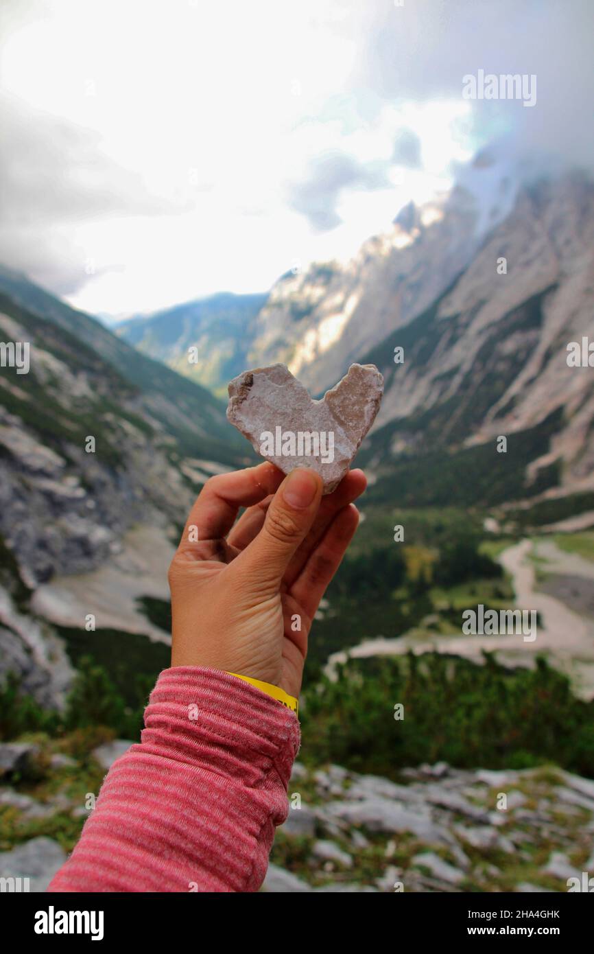woman holds a stone heart into the camera,above the reintal below the knorr hut,near garmisch-partenkirchen with a view of the reintalanger hut,garmisch-partenkirchen,wetterstein mountains,bavaria,germany,europe Stock Photo
