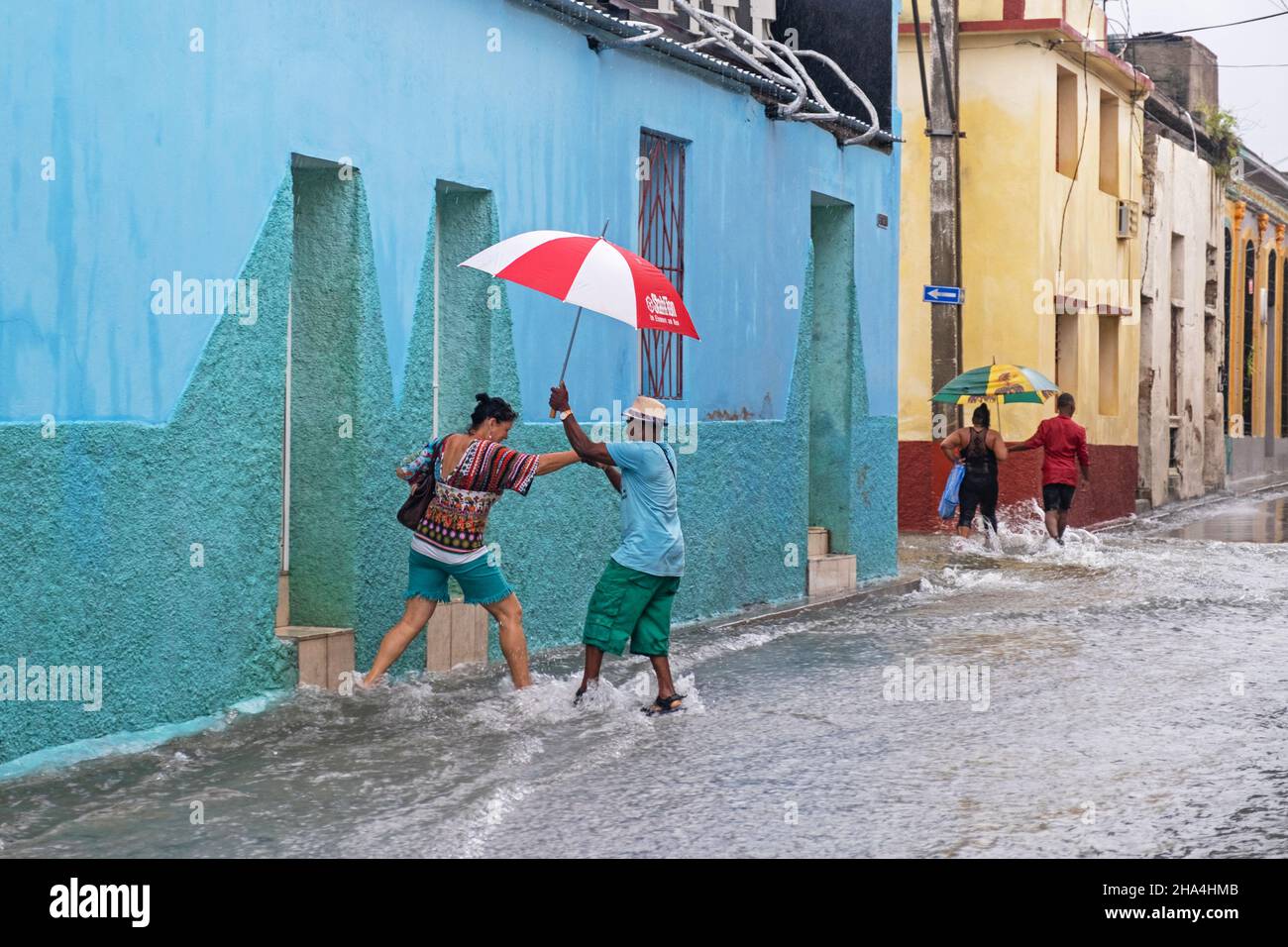 Cubans with umbrellas walking in flooded street during torrential rain in the city Santiago de Cuba on the island Cuba, Caribbean Stock Photo