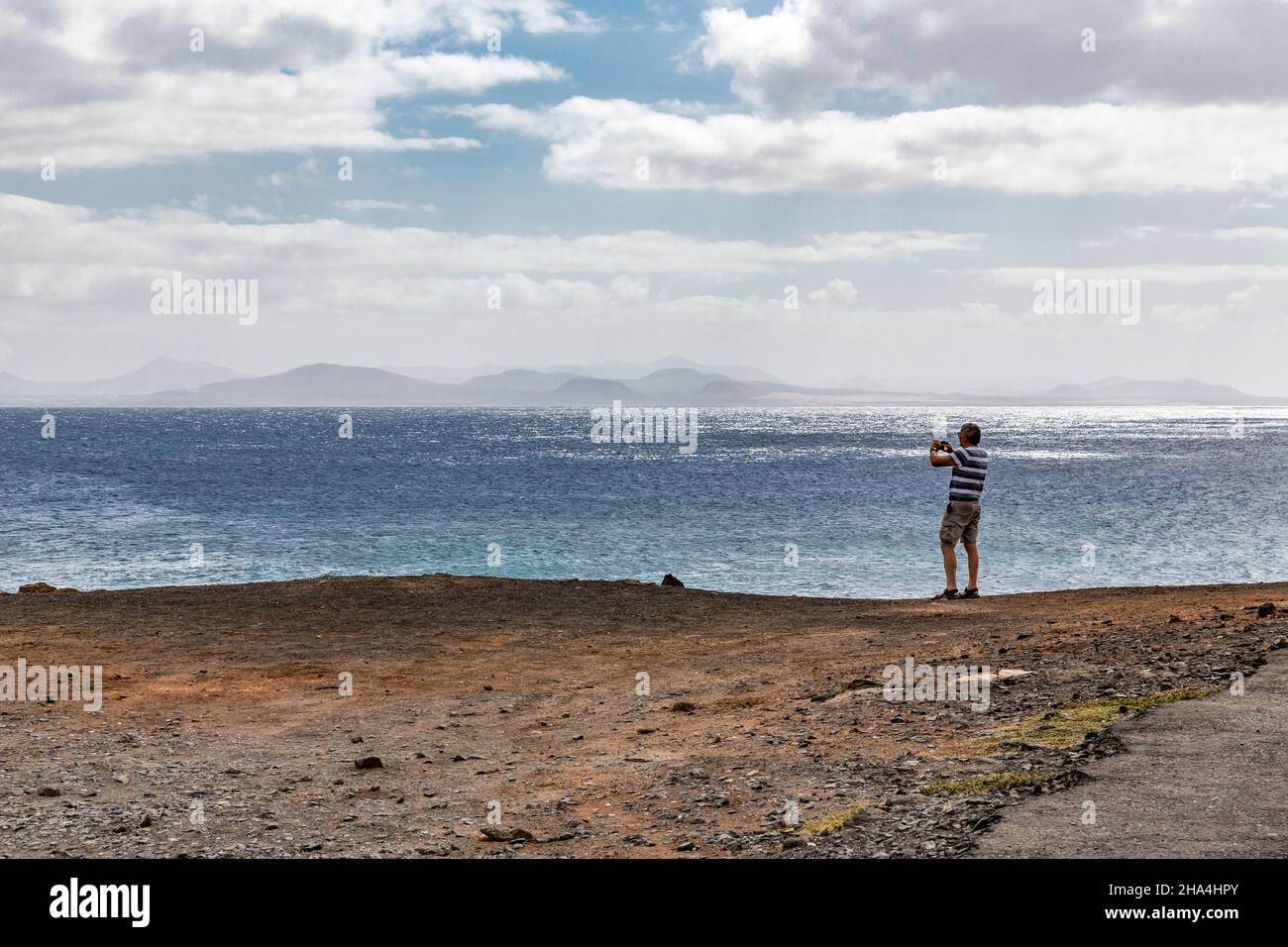 elderly man photographs the island of fuerteventura with a smartphone,punta pechiguera,playa blanca,lanzarote,canaries,canary islands,spain,europe Stock Photo
