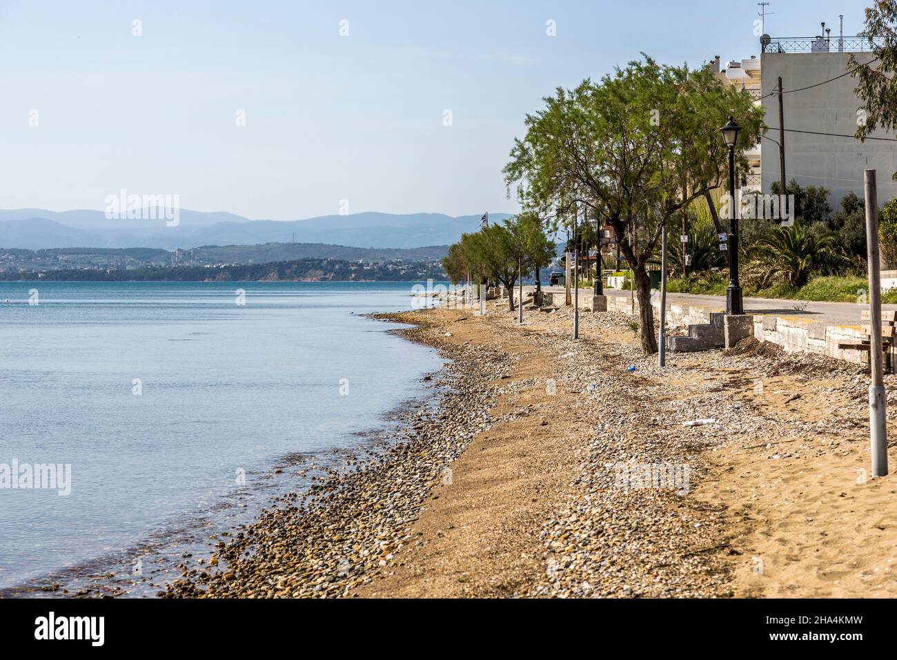 a sandy beach somewhere in greece. some rusty pegs coming out of the sand and enjoying the view sto the ocean and the mountains in the back. trees are also in the picture. Stock Photo
