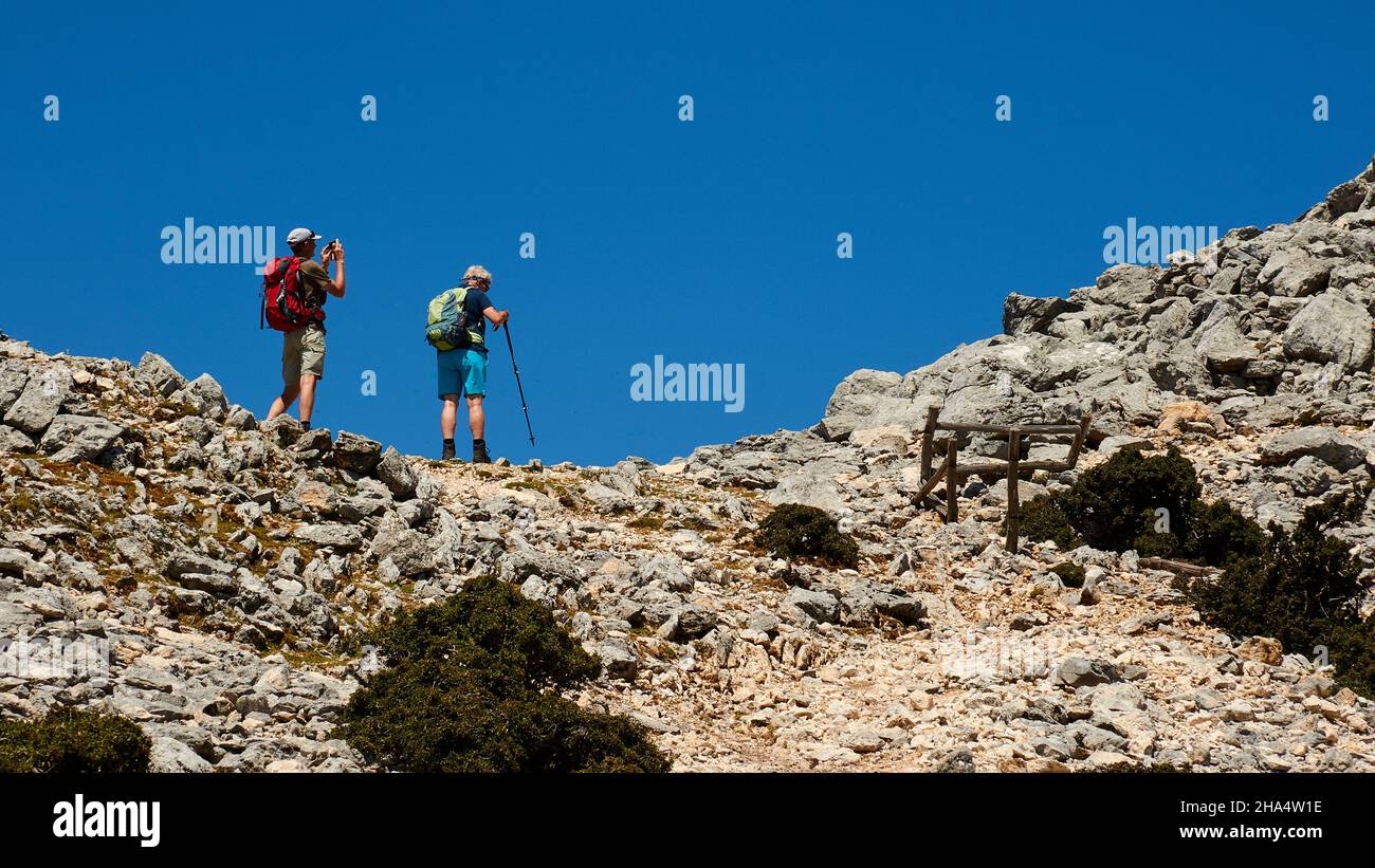 greece,greek islands,ionian islands,kefalonia,mountain,enos,summit,two hikers on the way to the summit,with hiking sticks,running on rocks,sky above blue without clouds Stock Photo