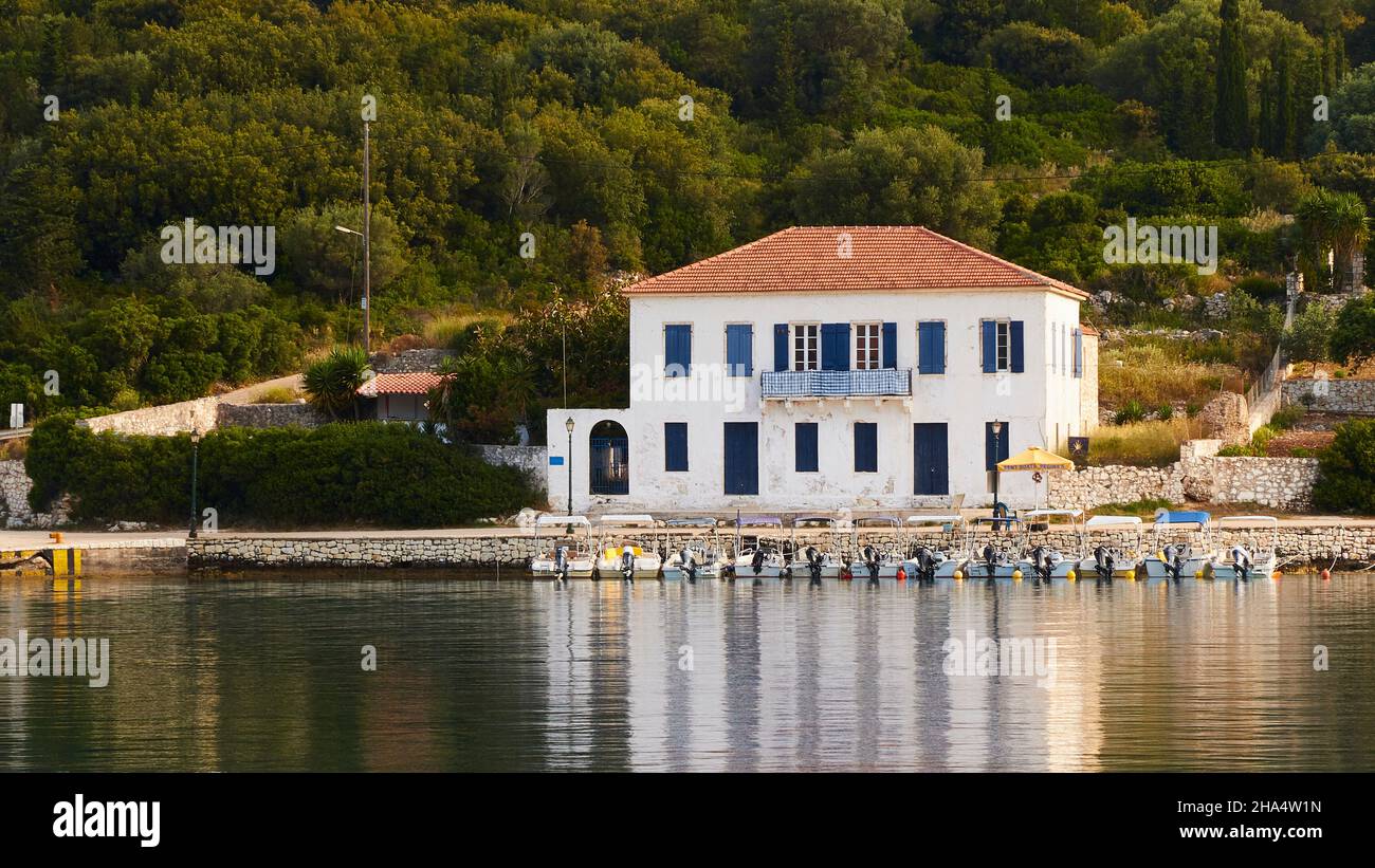 greece,greek islands,ionian islands,kefalonia,fiskardo,morning mood,partly cloudy sky,large white house with a red tiled roof,in front of it there are many small motor boats in the harbor basin,the house is reflected in the calm water Stock Photo