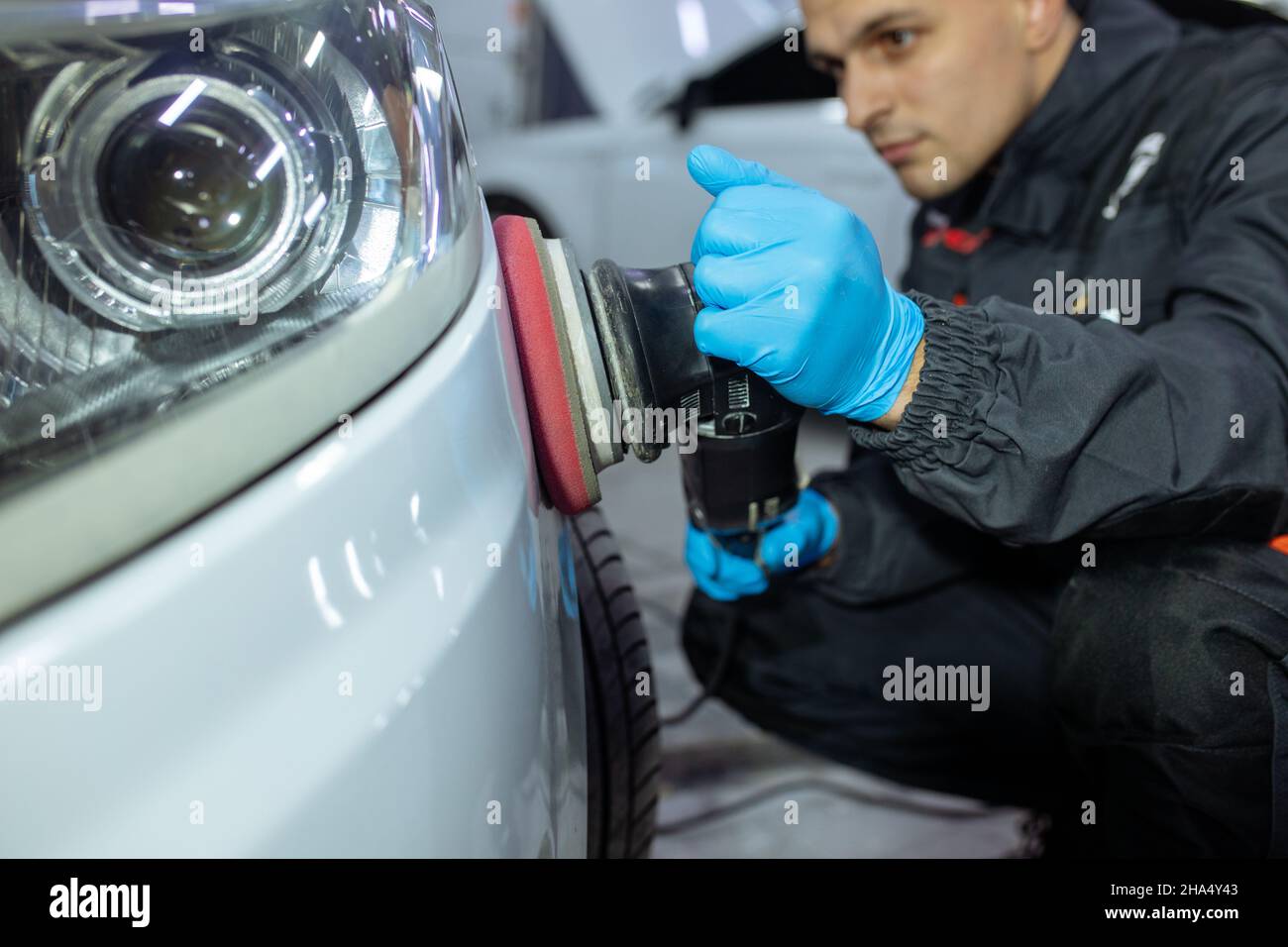 Serviceman polishing car body with machine in a workshop. Stock Photo