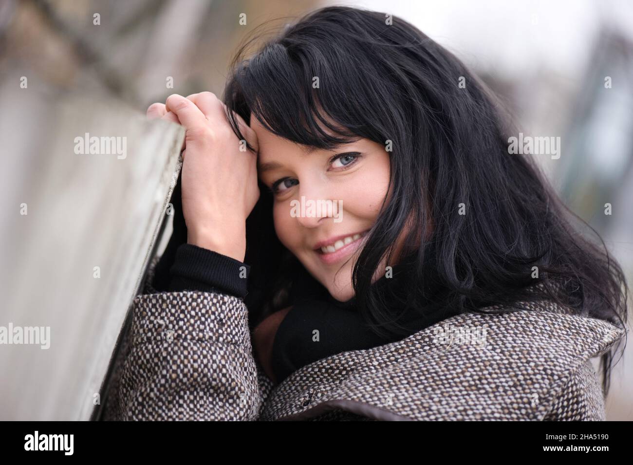 Smiling young woman in jacket standing beside old picket fence. Selective focus and shallow depth of field. Stock Photo
