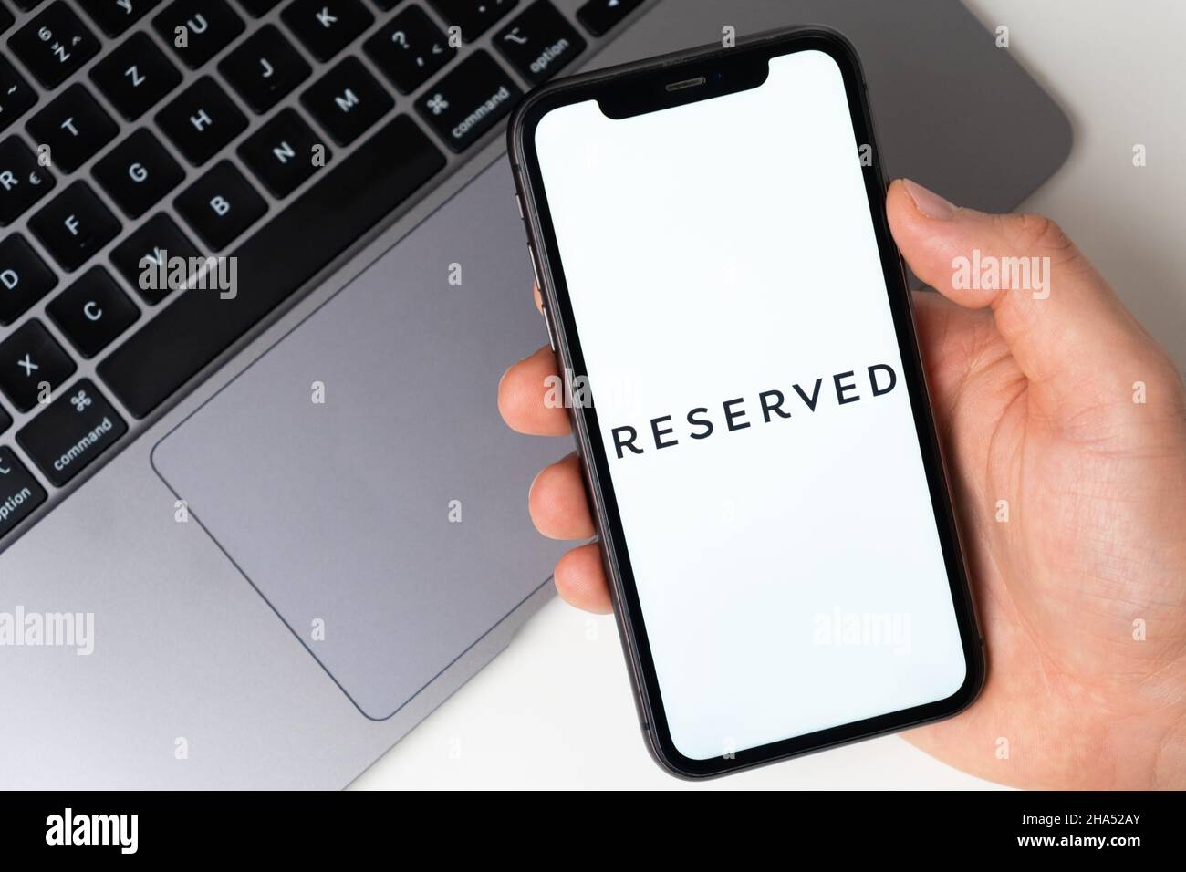 Reserved application logo for online shopping on the screen of mobile phone. Man hand holding a smartphone with application. November 2021, San Francisco, USA Stock Photo