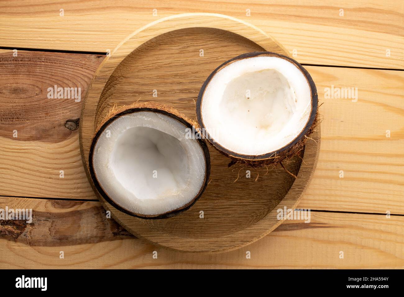 Two halves of fresh coconut on a wooden table, close-up, top view. Stock Photo