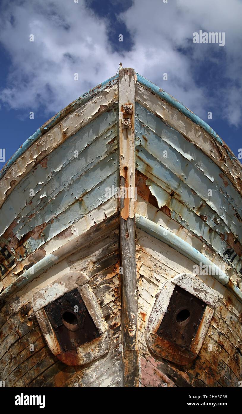 Old wooden ship painted with blue, paint peels off, against blue sky Stock Photo