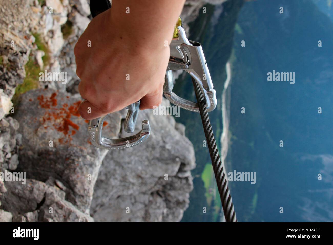 young woman on a mountain tour secures herself with a carabiner on a wire rope safety device over the mittenwalder höhenweg. germany,bavaria,upper bavaria,mittenwald, Stock Photo