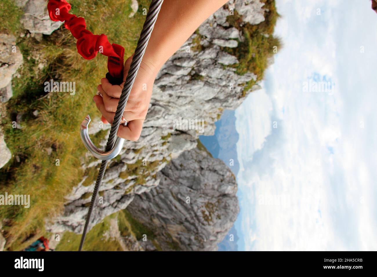 young woman during a mountain tour over the mittenwalder höhenweg secures herself with a carabiner on a wire rope,germany,bavaria,upper bavaria,mittenwald, Stock Photo