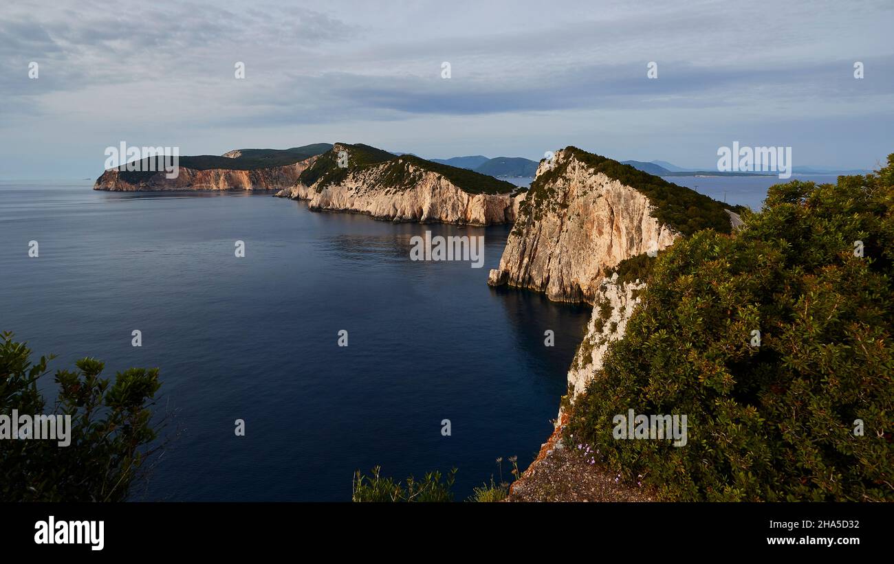 greece,greek islands,ionian islands,lefakada or lefkas,southern tip of the island,steep coast,cape lefkadas,afternoon light,wide-angle view,view from the lighthouse back to the north,green bushes on the right,dark blue sea,blue sky,strip of clouds Stock Photo