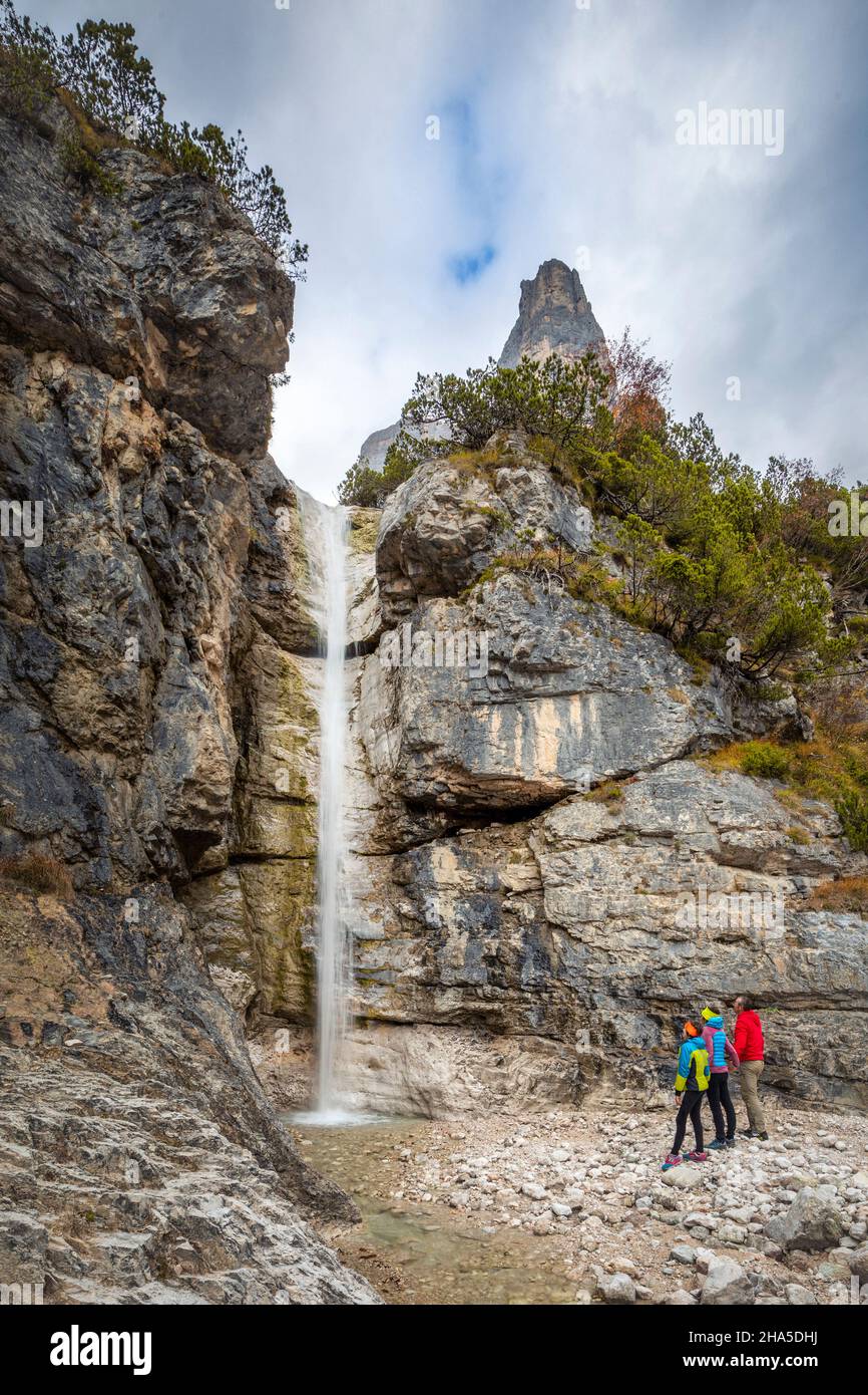 small family group (mother father and daughter) observes a small waterfall in the corpassa valley dominated by the trieste tower,civetta group,dolomites,taibon agordino,province of belluno,veneto,italy Stock Photo