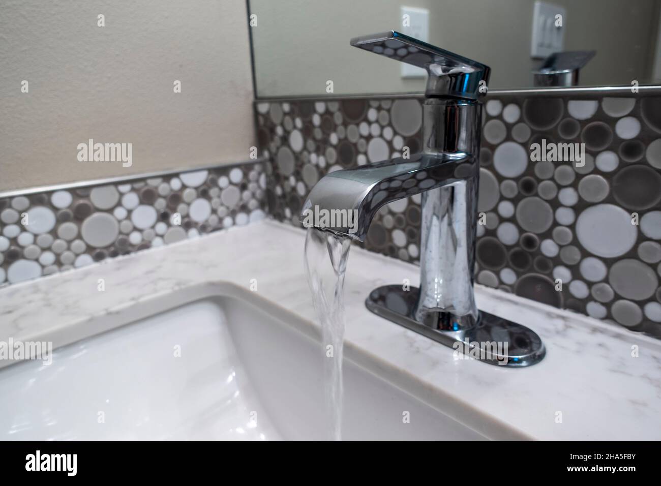 Close up view of a sink faucet inside an upscale bathroom, the water