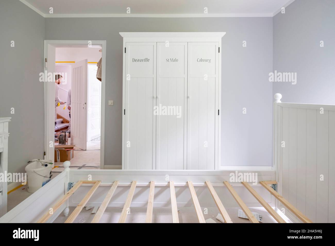 construction site,refurbishment and renovation of an apartment,bed frame in a freshly painted bedroom with craftsmen in the background Stock Photo