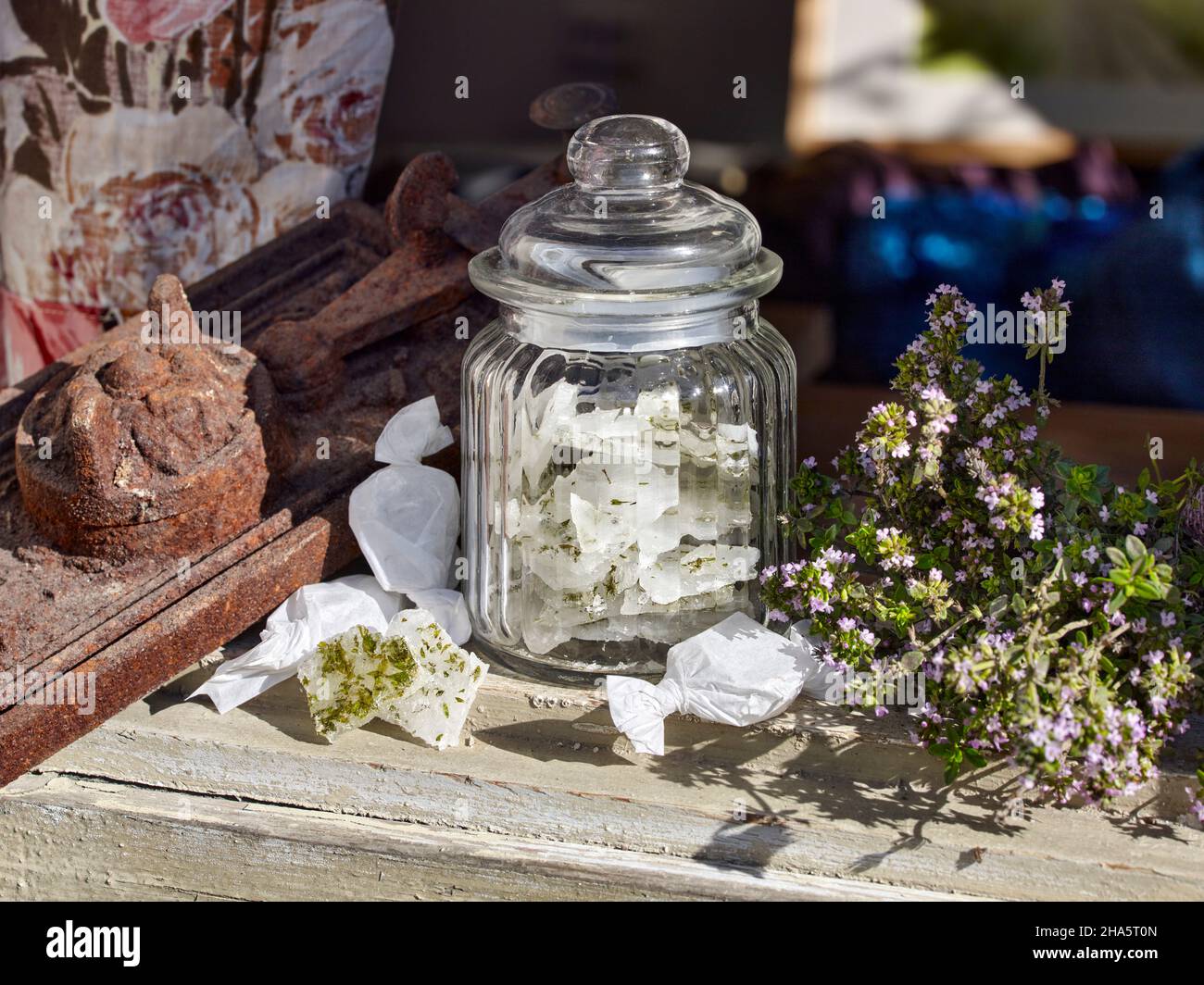 candy jar with lid,filled with thyme candies,on an old wooden window sill next to a bouquet of thyme and candies wrapped in paper Stock Photo