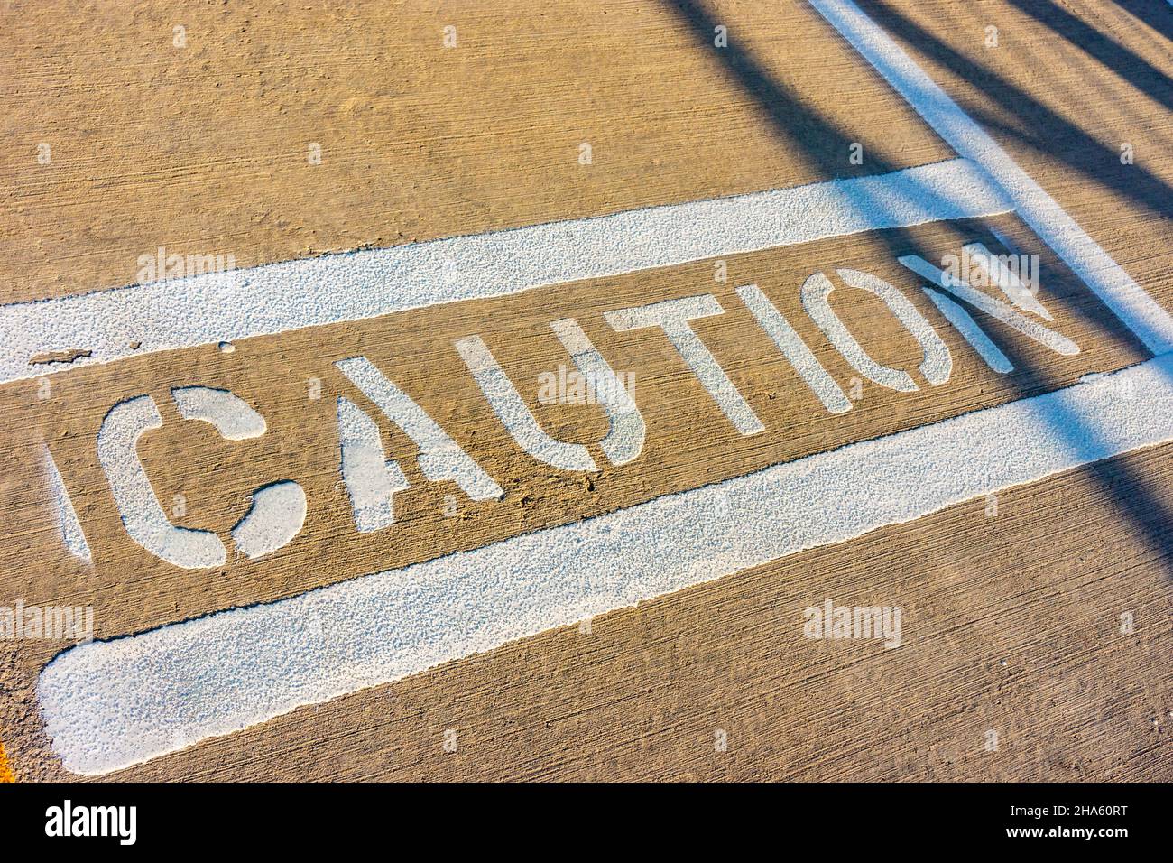 The word caution spelled out in white paint on the sidewalk. Stock Photo