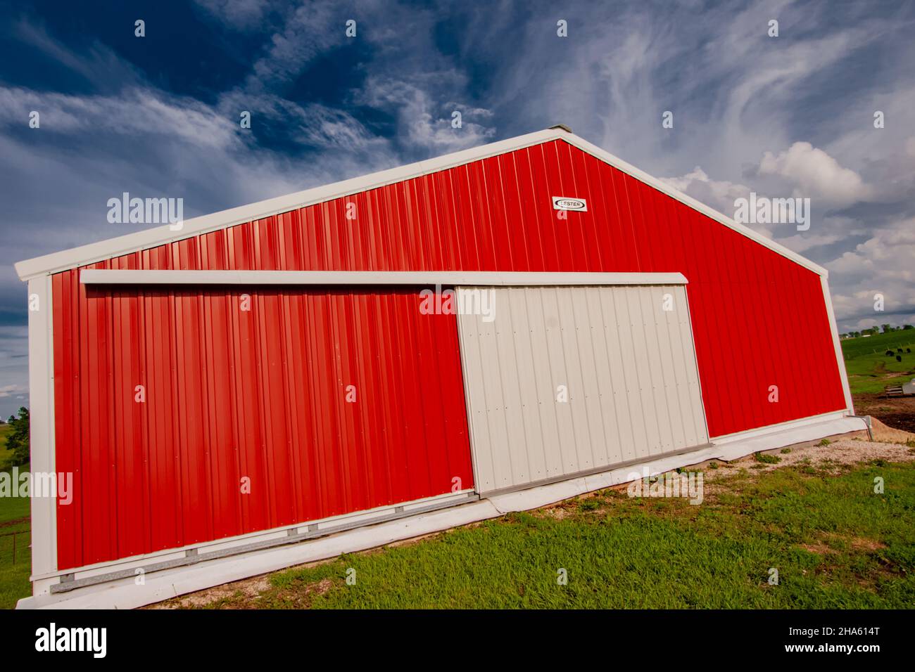 Red and white Lester pole barn in a field of Green grass and under a blue sky with fluffy clouds. Stock Photo