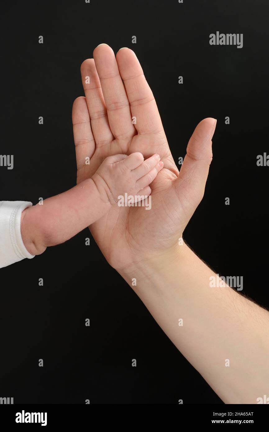 Roughness and texture on the skin of the palm of the hand of a Caucasian person against the hand of a baby. Hands isolated on black background. Stock Photo