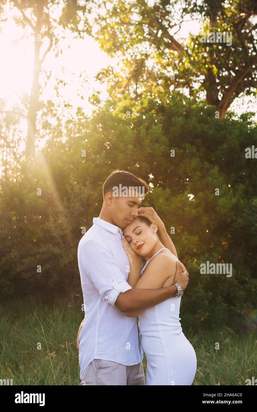Vertical shot of 2 young lovers embraced in a forest at sunset Stock Photo
