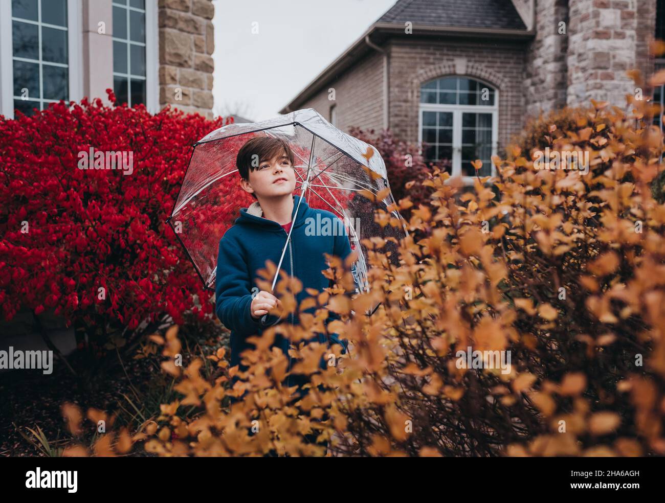 Boy holding umbrella in front of house on a rainy fall day. Stock Photo