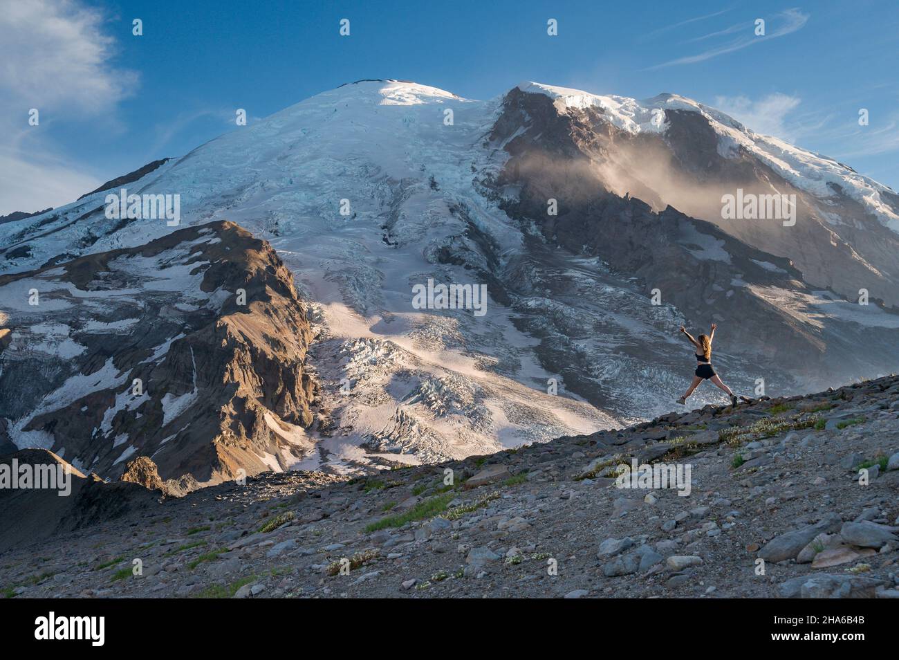 Fit female jumping with excitement on a ridge next to Mount Rainier Stock Photo