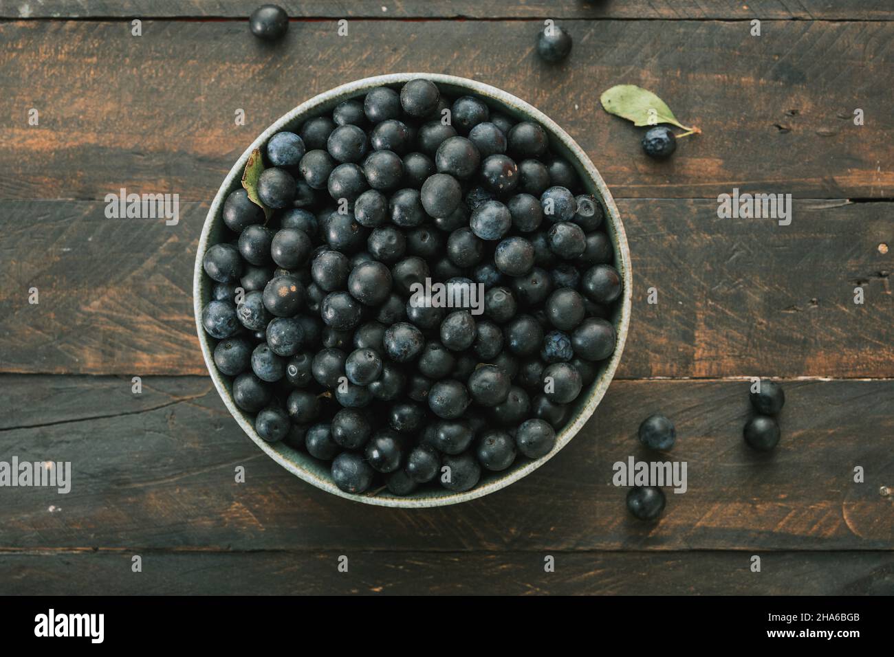 A bowl with sloe (prunus spinosa) black-bluish fruis on dark rustic wooden table background Stock Photo