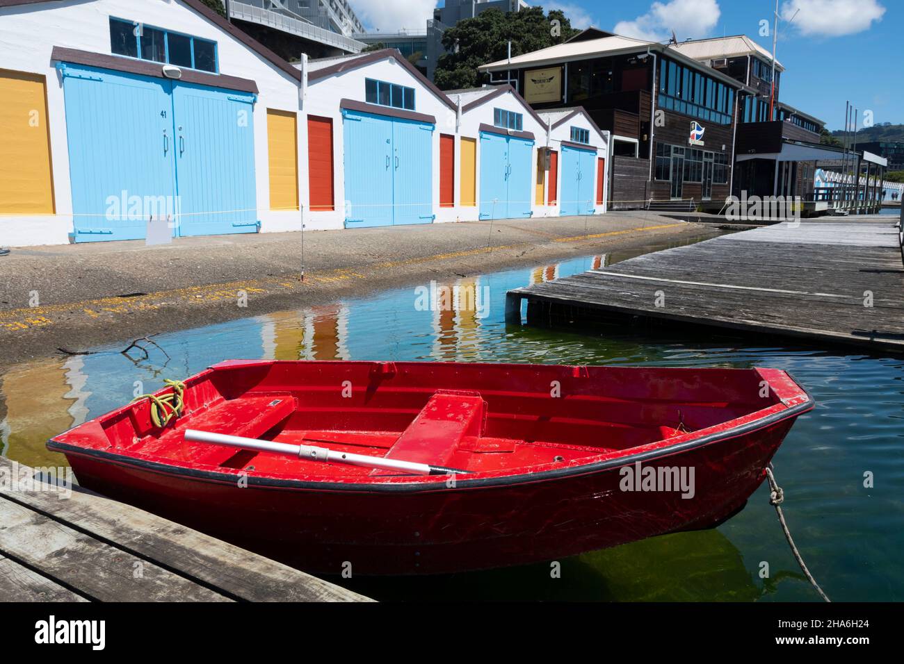 Red dingy in front of Blue boat sheds, Boat Harbour, Wellington, North Island, New Zealand Stock Photo