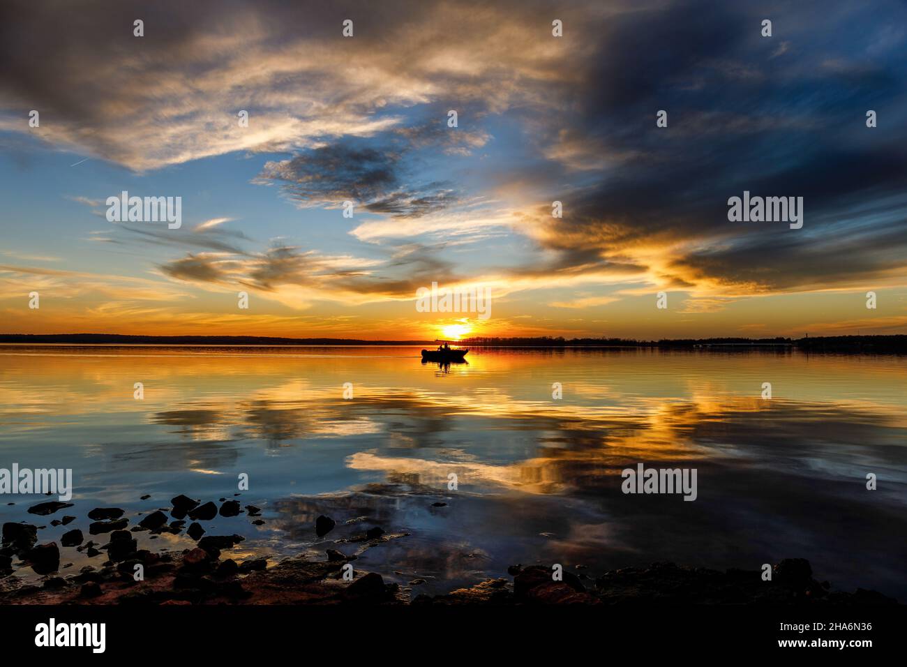 A boat on the lake at sunset with the clouds reflecting in the water. Stock Photo