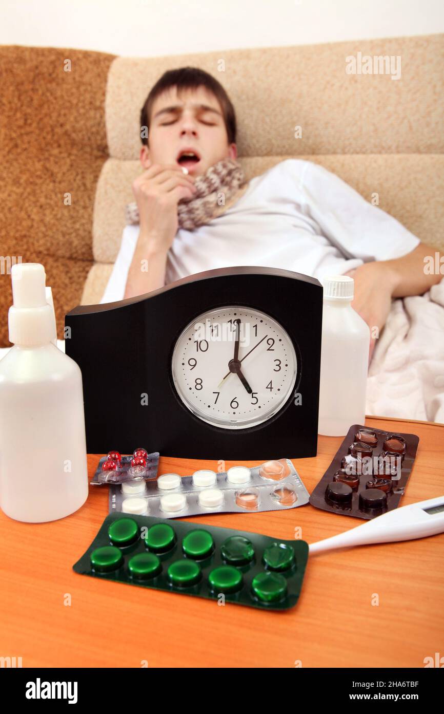 Focus on the Clock. Sick Teenager taking a Pill on the Bed at the Home Stock Photo