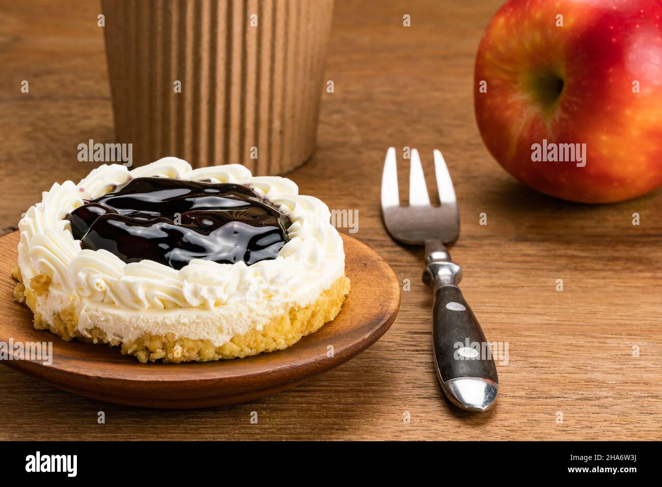Delicious healthy breakfast of Blueberry Cheese Pie on wooden plate with metal fork, coffee cup and ripe red apple on wooden table. Stock Photo