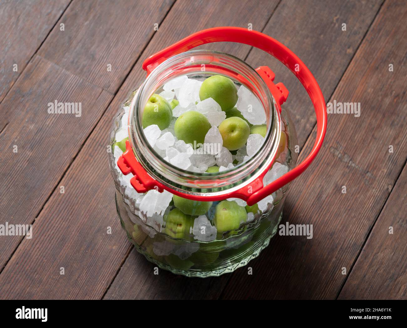 Unripe ume fruit and rock sugar on a wooden background.Making traditional japanese green plum wine Stock Photo