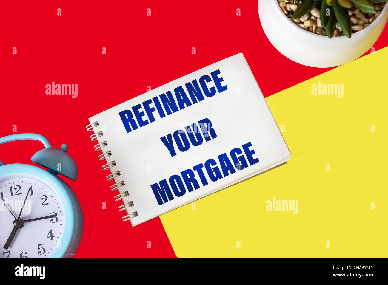 Text Refinance your mortgage, written on a notepad and a red and yellow background with a clock and a cactus Stock Photo