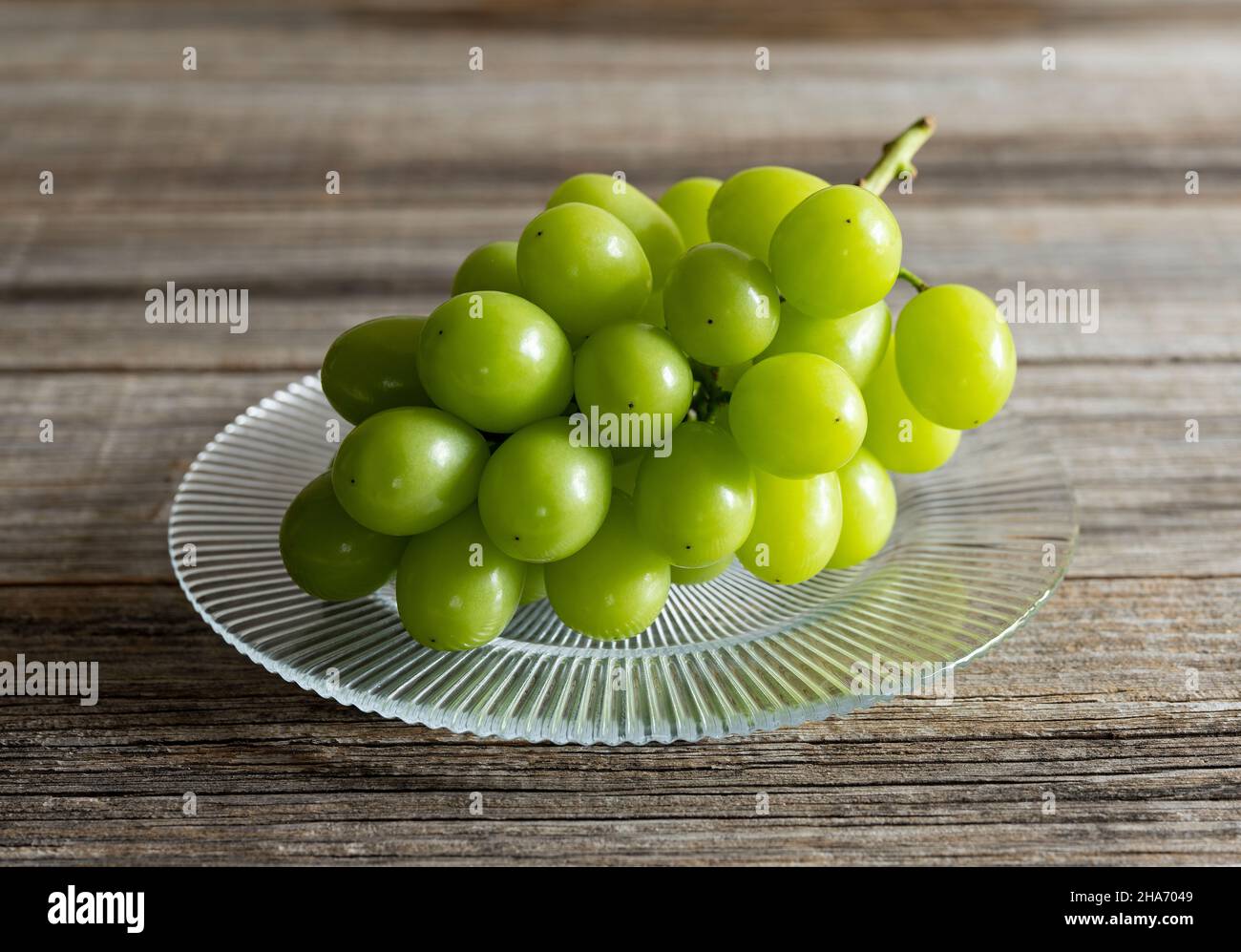 Shine Muscat grapes on a glass plate set against a wooden background