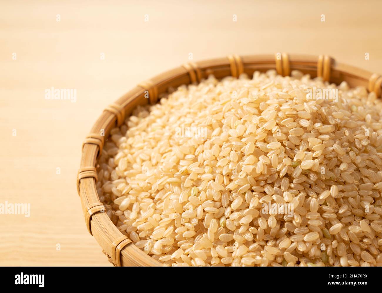 Brown rice in a bamboo colander set against a wooden background. A pile ...