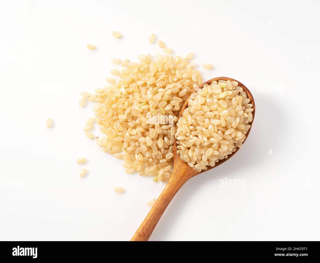 Brown rice in a wooden spoon placed on a white background. A pile of