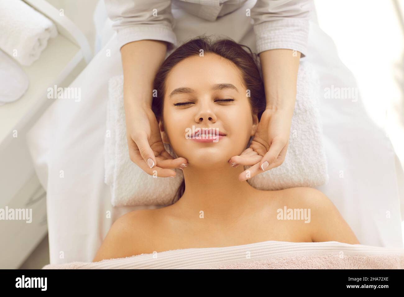 Happy relaxed woman getting facial skin treatment and face massage at spa center Stock Photo