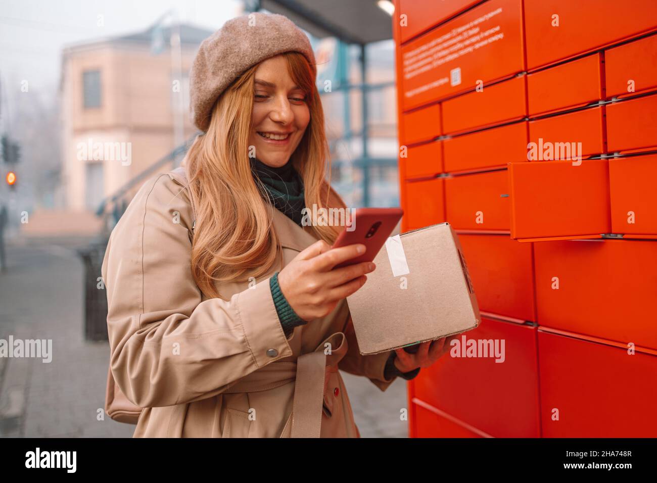 Young caucasian woman received parcel using automated self-service post terminal machine. Freight transportation. Express delivery. Stock Photo