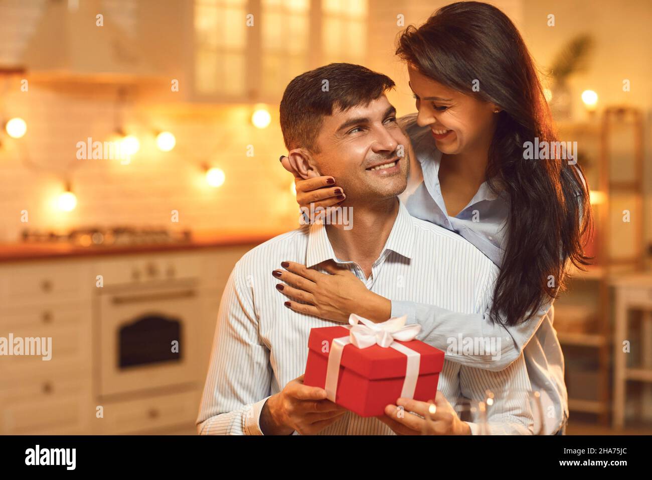 Joyful excited man received a gift from his girlfriend, who stands behind him and hugs him. Stock Photo