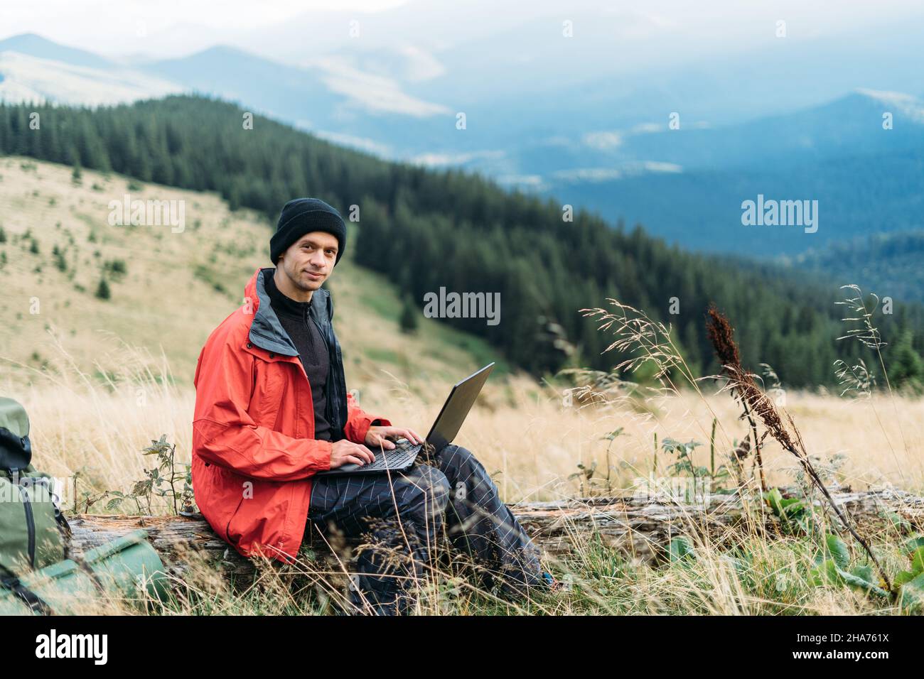 man working outdoors with laptop sitting in the mountains. Remote work or freelance lifestyle concept. Broadband cellular coverage. 5G Internet Stock Photo
